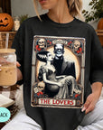 A woman wearing a black t-shirt with a graphic design featuring a couple and the text "MONSTER THE LOVERS". She is holding a drink in her hand.