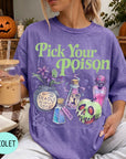 A woman wearing a purple t-shirt with a Halloween-themed design, holding a drink and surrounded by Halloween decorations.