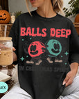 A person wearing a black t-shirt with a graphic design of two cartoon characters and the text "BALLS DEEP" printed on it, holding a drink.