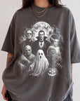 A person wearing a gray t-shirt with a graphic design featuring various Halloween-themed characters, including Dracula, Frankenstein, Frankenstein's Bride, Mummy, and a ghost.