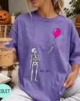 A woman wearing a purple t-shirt with a skeleton holding a pink balloon and the text "Well, shit..." printed on it.
