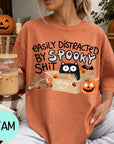 A woman wearing a t-shirt with a humorous Halloween-themed graphic, including a cat, pumpkin, and text that says "EASILY DISTracted BY SPOOKY SHIT".