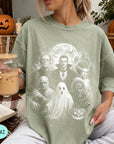 A woman wearing a green t-shirt with a Halloween-themed graphic of characters from the horror film "The Exorcist" is holding a glass of iced coffee.