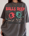 A person wearing a gray t-shirt with a graphic design featuring two cartoon characters, one red and one green, along with the text "BALLS DEEP" and "IN CHRISTMAS SPIRIT".