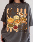 A person wearing a gray t-shirt with a graphic design depicting various Thanksgiving dishes and the text "SIDE CHICK SOCIAL CLUB" printed on it.