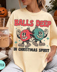 A person wearing a yellow t-shirt with a graphic design of two cartoon characters, one red and one green, along with the text "BALLS DEEP IN CHRISTMAS SPIRIT". The person is holding a drink in a glass with a straw.