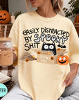 A person wearing a yellow t-shirt with a humorous Halloween-themed graphic, including a cat, pumpkin, and text that says "EASILY DISTracted BY SPOOKY SHIT".