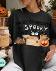 A person wearing a black t-shirt with a Halloween-themed graphic and text, holding a drink in a glass.