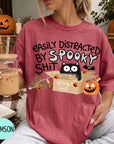 A woman wearing a red t-shirt with a Halloween-themed graphic and text, holding a drink in a glass.