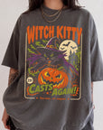 A person wearing a gray t-shirt with a Halloween-themed graphic design featuring a witch, a jack-o-lantern, and bats.