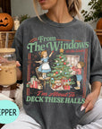 A woman wearing a gray t-shirt with a graphic design of a Christmas tree and two children decorating it, holding a drink in a glass.