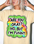 A person wearing a yellow t-shirt with a colorful graphic and text that says "ARE YOU OKAY? NO, BUT I&