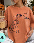 A woman wearing an orange t-shirt with a skeleton drawing and the word "boop" printed on it, holding a glass of iced coffee.