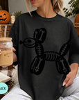 A woman wearing a black t-shirt with a skeleton dog design is sitting on a couch, holding a drink in a glass with a straw.