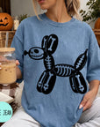 A woman wearing a blue t-shirt with a skeleton dog graphic is sitting on a couch, holding a drink in a glass.