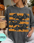 A woman wearing a gray t-shirt with a graphic of bats and stars is sitting on a couch, holding a drink in a glass.