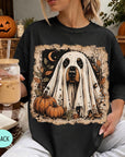 A woman wearing a black t-shirt with a Halloween-themed graphic of a ghost dog, holding a drink and surrounded by pumpkins and a jack-o-lantern.