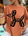 A woman wearing an orange t-shirt with a skeleton dog graphic is sitting on a couch, holding a drink in a glass.