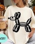 A woman wearing a white t-shirt with a skeleton dog graphic is sitting on a couch, holding a glass of iced coffee.