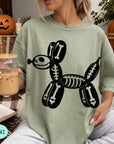 A woman wearing a green t-shirt with a skeleton dog graphic is sitting on a couch, holding a glass of iced coffee.