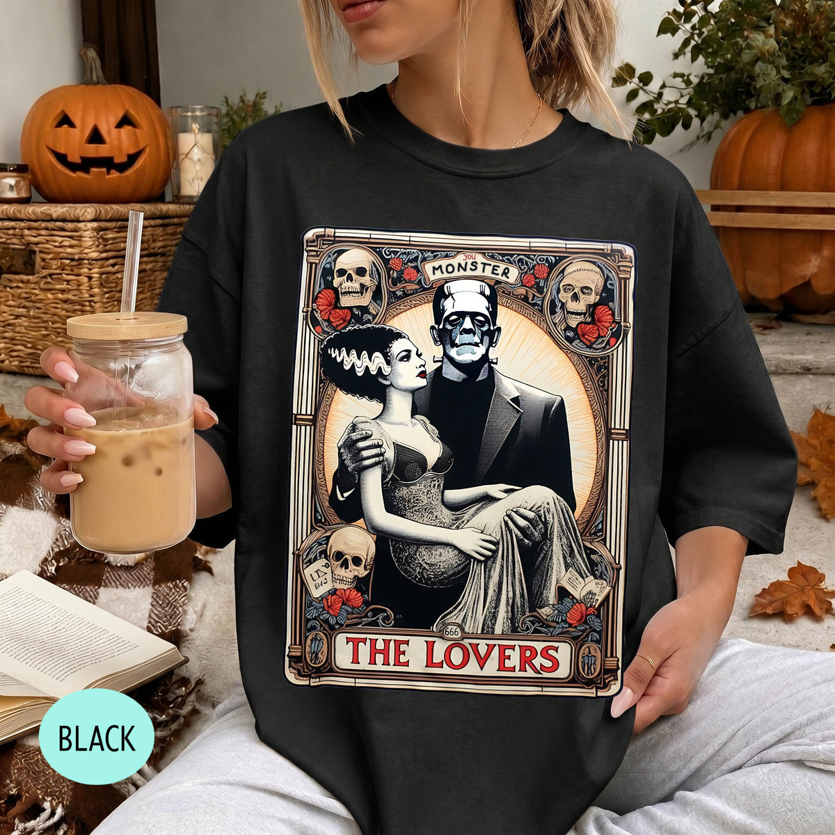 A woman wearing a black t-shirt with a graphic design featuring a couple and the text "MONSTER THE LOVERS". She is holding a drink in her hand.