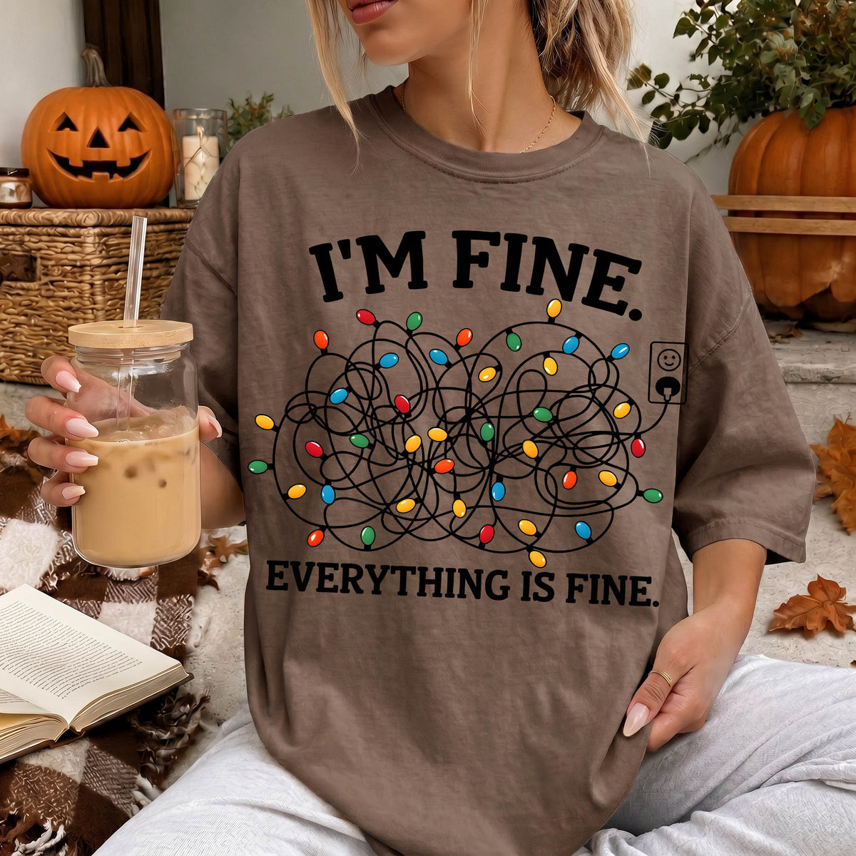 A person wearing a t-shirt with a humorous text and a graphic design, sitting in a cozy setting with a pumpkin and other fall decorations in the background.