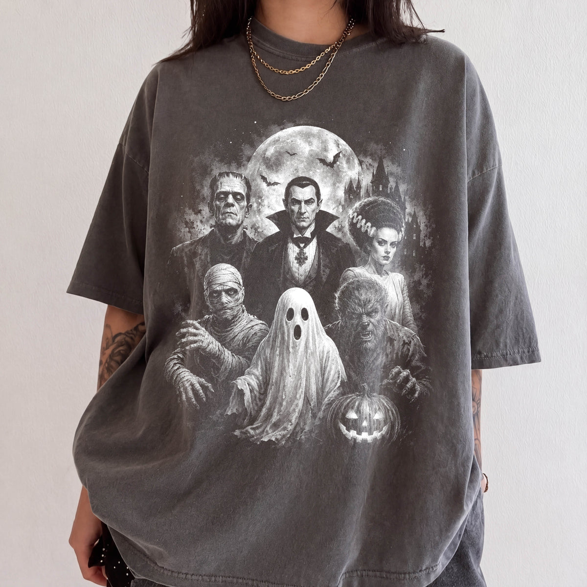 A person wearing a gray t-shirt with a graphic design featuring various Halloween-themed characters, including Dracula, Frankenstein, Frankenstein's Bride, Mummy, and a ghost.