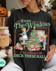 A woman wearing a black t-shirt with a graphic design depicting a Christmas tree and two children decorating it. She is holding a drink in her hand.