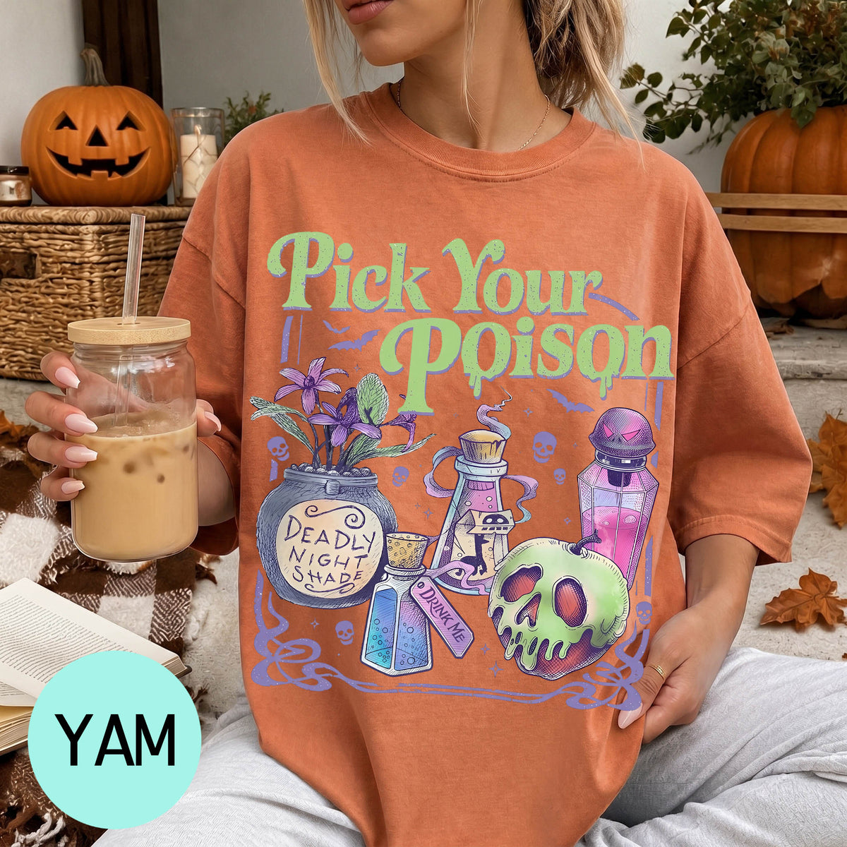 A woman wearing a t-shirt with a Halloween-themed graphic and holding a drink, with a pumpkin and other Halloween decorations visible in the background.
