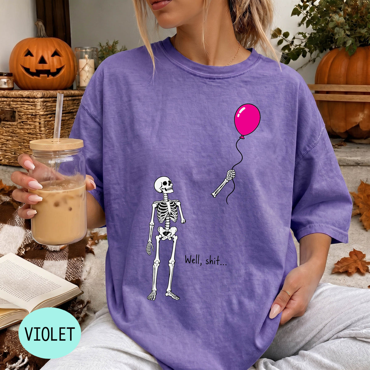 A woman wearing a purple t-shirt with a skeleton holding a pink balloon and the text "Well, shit..." printed on it.