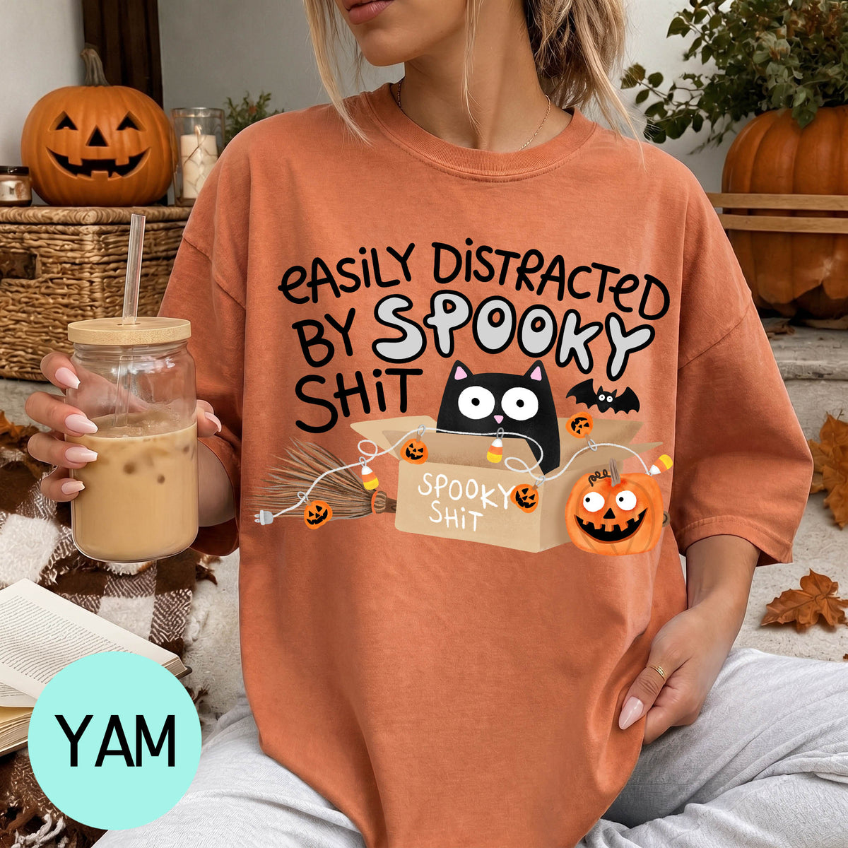 A woman wearing a t-shirt with a humorous Halloween-themed graphic, including a cat, pumpkin, and text that says "EASILY DISTracted BY SPOOKY SHIT".