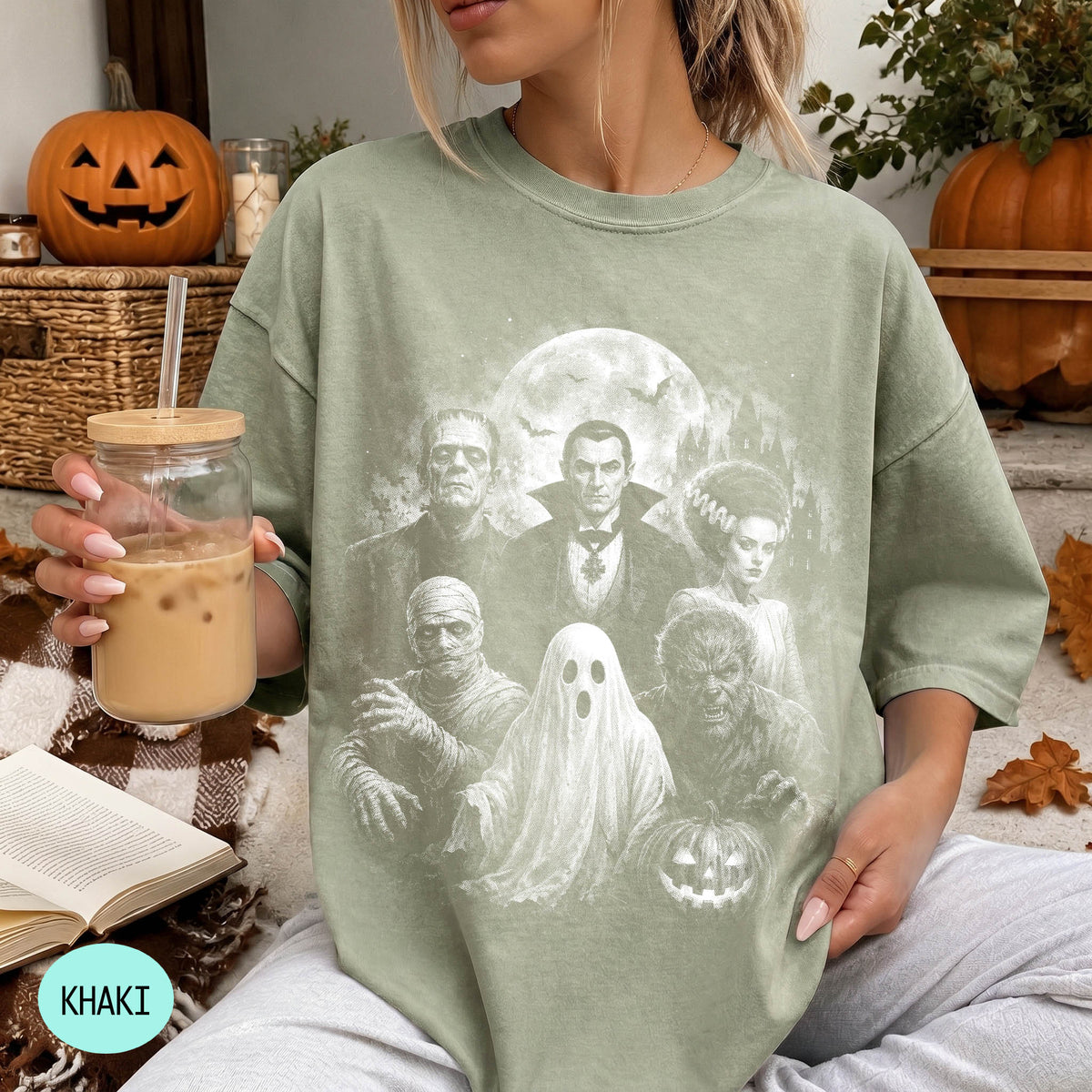 A woman wearing a green t-shirt with a Halloween-themed graphic of characters from the horror film "The Exorcist" is holding a glass of iced coffee.