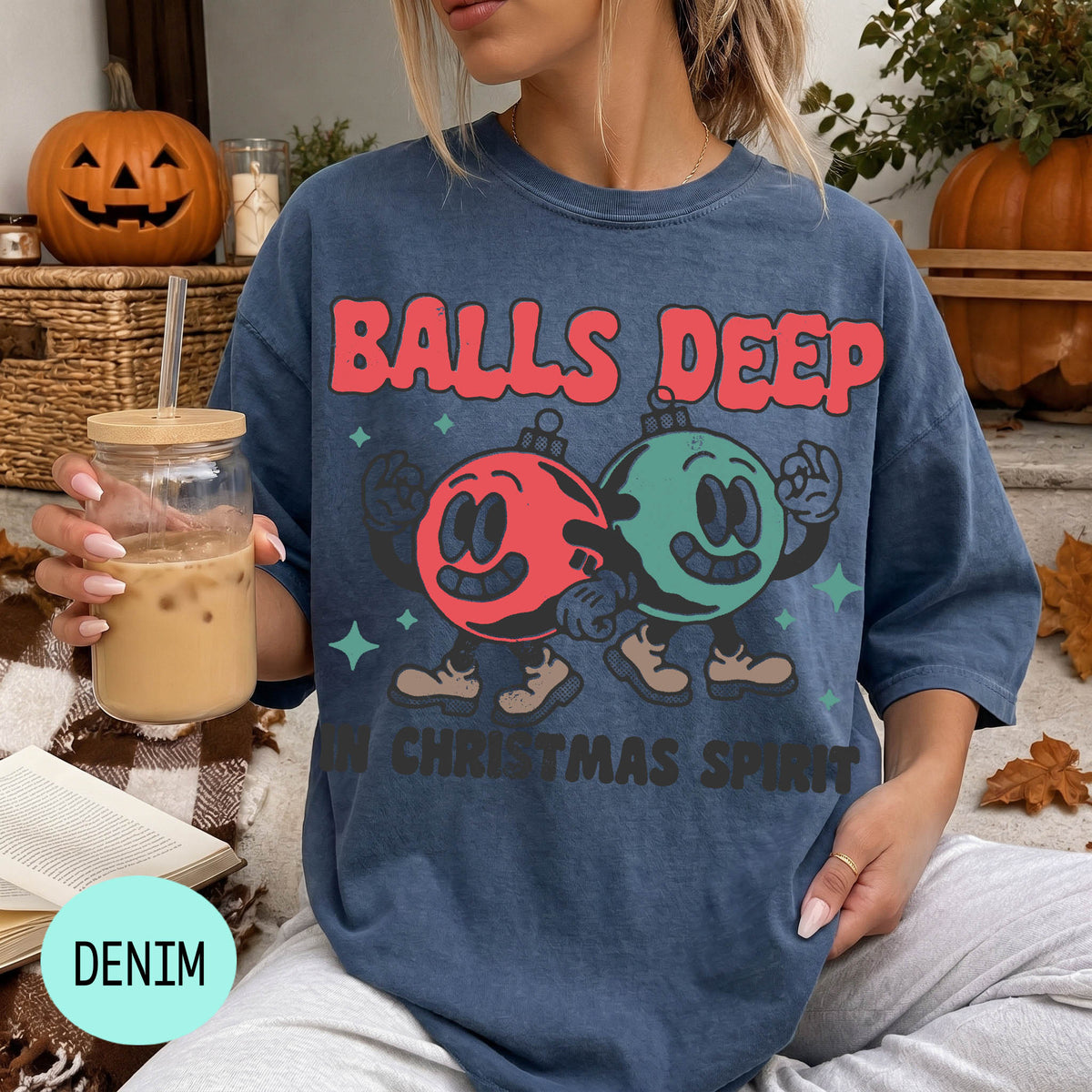 A woman wearing a blue t-shirt with a graphic design of two cartoon characters, one red and one green, holding a drink and surrounded by Halloween decorations.