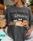 A woman wearing a gray t-shirt with a Halloween-themed graphic and text, holding a drink in a glass.