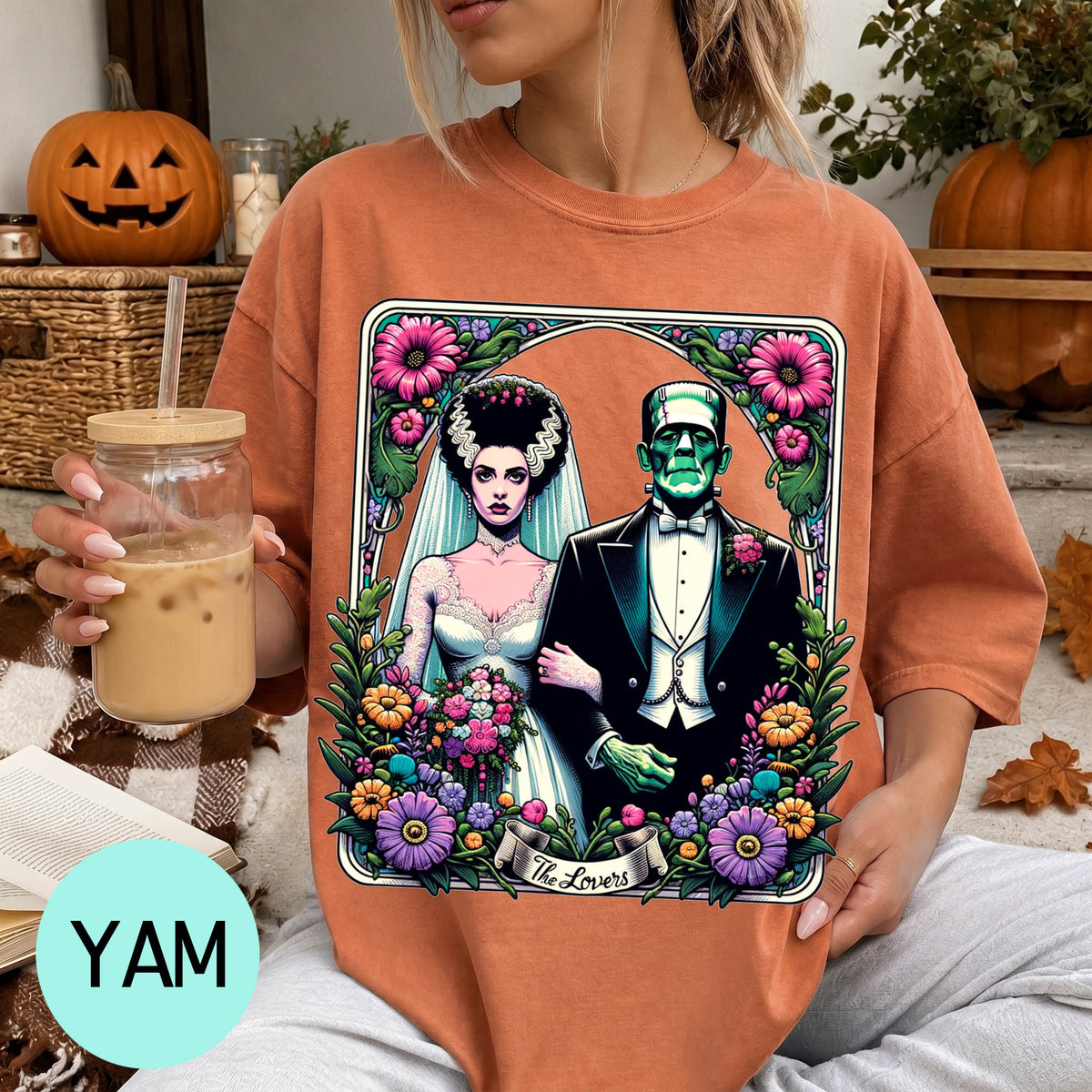 A woman wearing a t-shirt with a graphic design of a bride and a Frankenstein monster, surrounded by flowers and leaves.