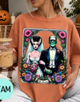 A woman wearing a t-shirt with a graphic design of a bride and a Frankenstein monster, surrounded by flowers and leaves.