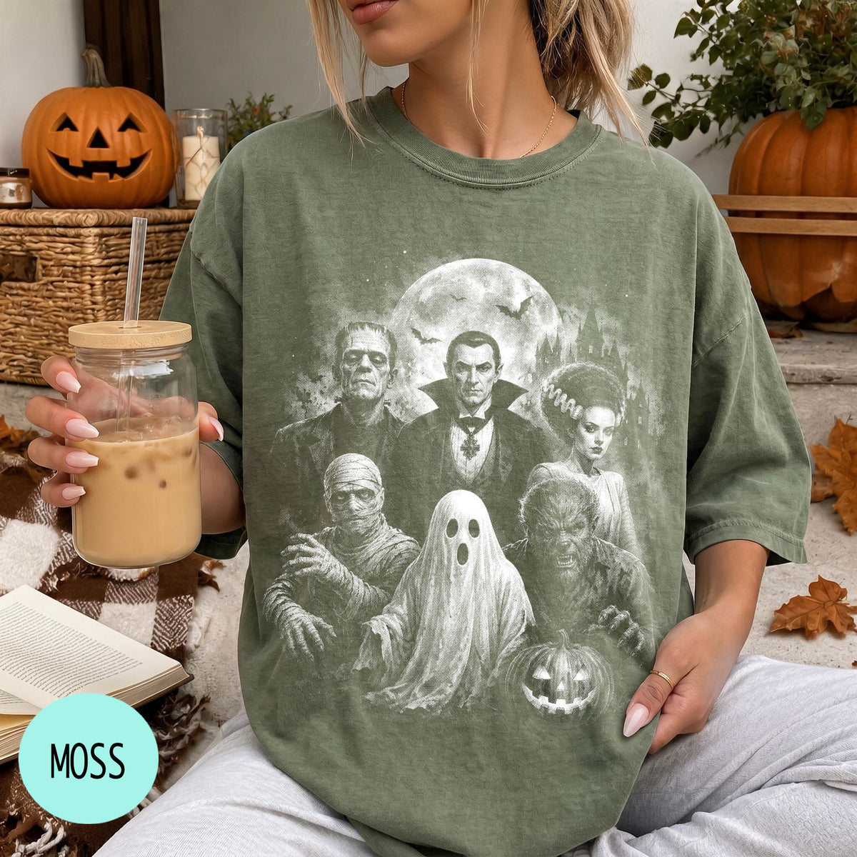 A person is sitting on a couch, wearing a green t-shirt with a Halloween-themed graphic of characters from the classic horror film "The Exorcist". The person is holding a drink in a glass with a straw.