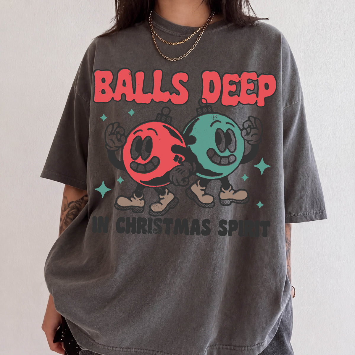 A person wearing a gray t-shirt with a graphic design featuring two cartoon characters, one red and one green, along with the text "BALLS DEEP" and "IN CHRISTMAS SPIRIT".