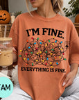 A woman wearing a t-shirt with a humorous graphic and text, sitting on a couch with a pumpkin and a mug of iced coffee in the background.