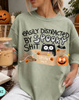 A woman wearing a green t-shirt with a humorous Halloween-themed graphic, including a cat, pumpkins, and bats, along with the text "EASILY DISTracted BY SPOKEY SHIT".