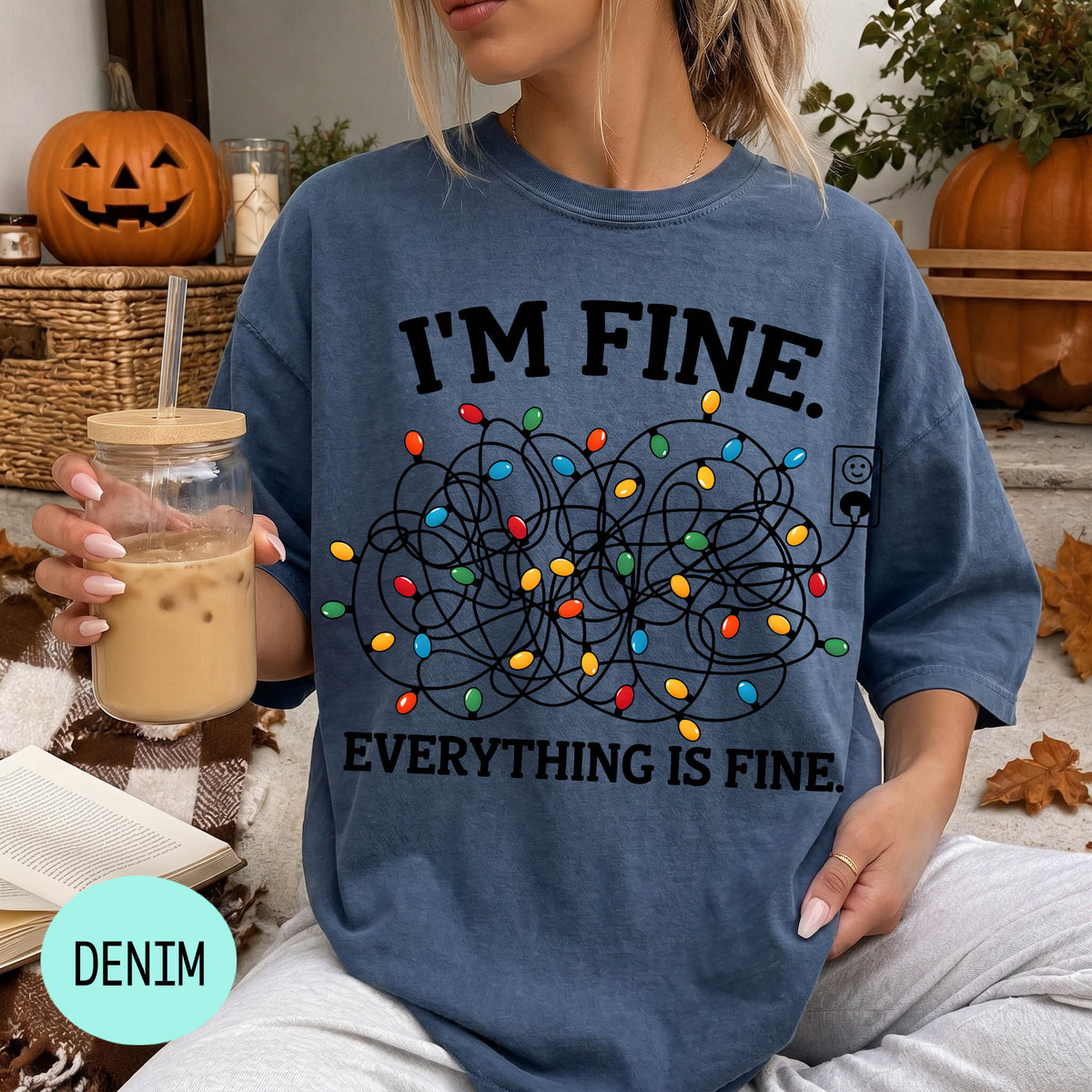 A woman wearing a blue t-shirt with a graphic design of colorful lights and the text "I'm Fine. EVERYTHING IS FINE." She is holding a drink in a glass with a straw.