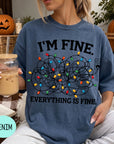A woman wearing a blue t-shirt with a graphic design of colorful lights and the text "I'm Fine. EVERYTHING IS FINE." She is holding a drink in a glass with a straw.