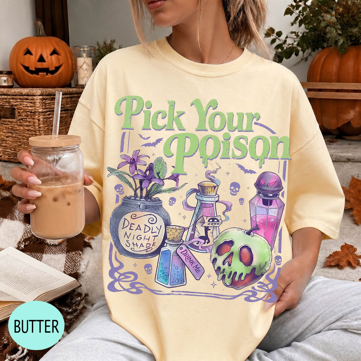 A woman wearing a yellow t-shirt with a graphic design featuring Halloween-themed elements such as a skull, a bottle, and a pumpkin. She is holding a drink in a glass with a straw.