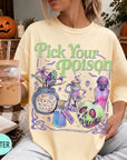 A woman wearing a yellow t-shirt with a graphic design featuring Halloween-themed elements such as a skull, a bottle, and a pumpkin. She is holding a drink in a glass with a straw.