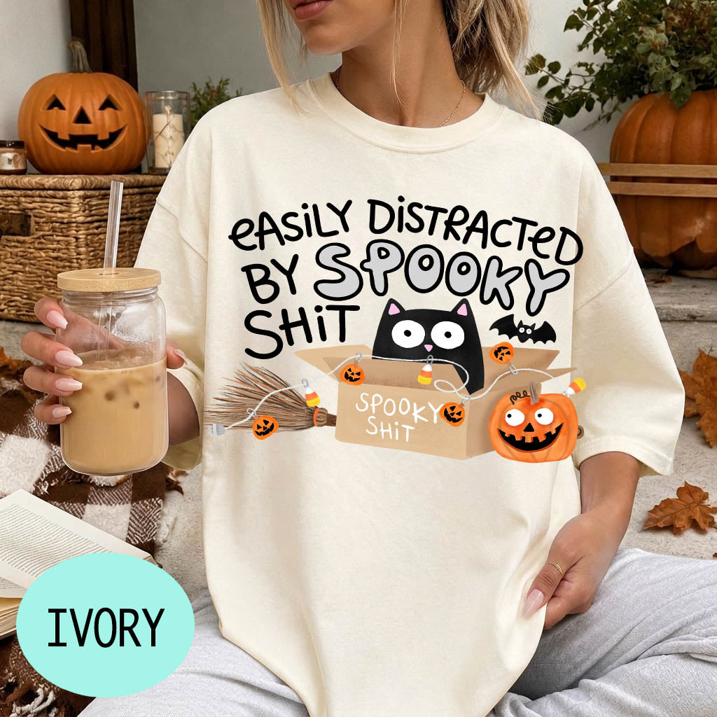 A person wearing a white t-shirt with a humorous Halloween-themed graphic and text, holding a drink in a glass.