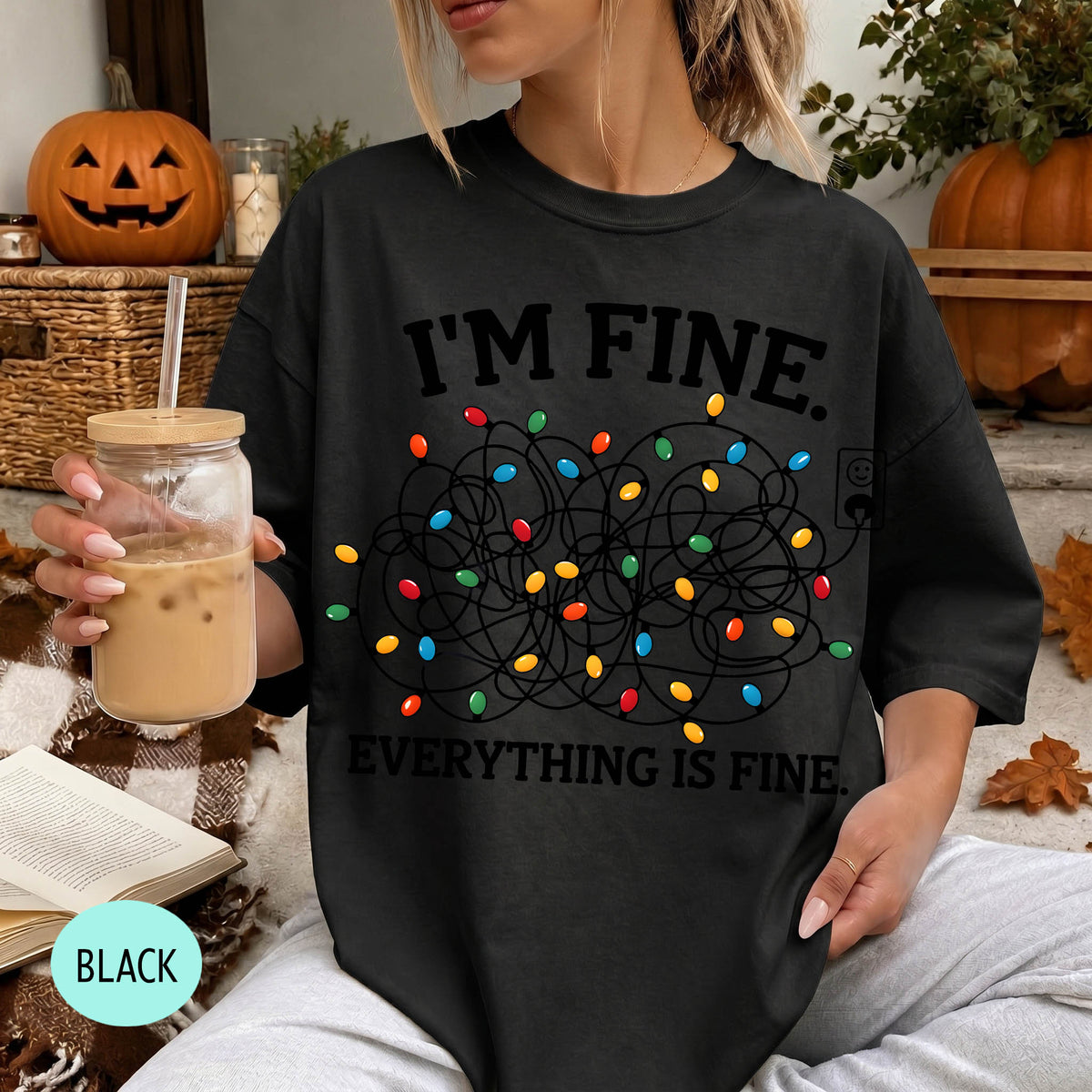A woman wearing a black t-shirt with a graphic design of colorful lights and the text "I'm Fine. Everything is Fine." She is holding a drink in a glass with a straw.