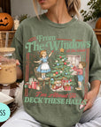 A woman wearing a green t-shirt with a Christmas-themed illustration and text, holding a glass of iced coffee.