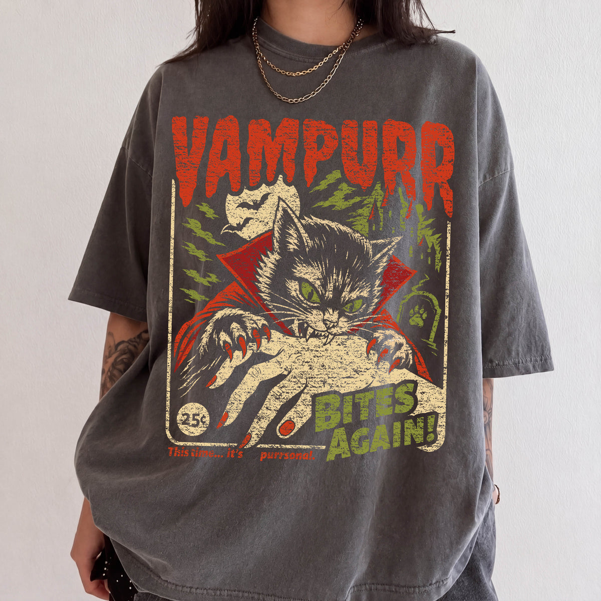 A person wearing a gray t-shirt with a graphic design featuring a cat with a bat-like face and the text "VAMPURR BITE'S AGAIN!"