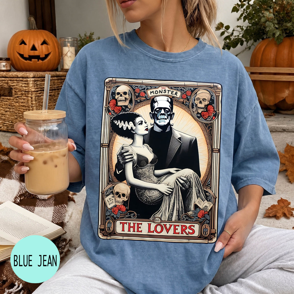 A woman wearing a blue t-shirt with a graphic design featuring a couple and the text "MONSTER THE LOVERS". She is holding a drink in a glass with a straw.