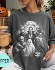 A woman wearing a t-shirt with a Halloween-themed graphic of the classic horror movie characters, including Frankenstein, Dracula, Frankenstein's monster, Frankenstein's ghost, and the werewolf. She is holding a drink in a glass with a straw.